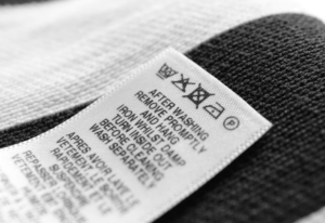 Close-up of a clothing care tag showing laundry symbols for washing, drying, ironing, and dry cleaning—useful for understanding fabric labels.